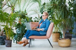 Urban jungle at home office, woman with laptop work among green plants.