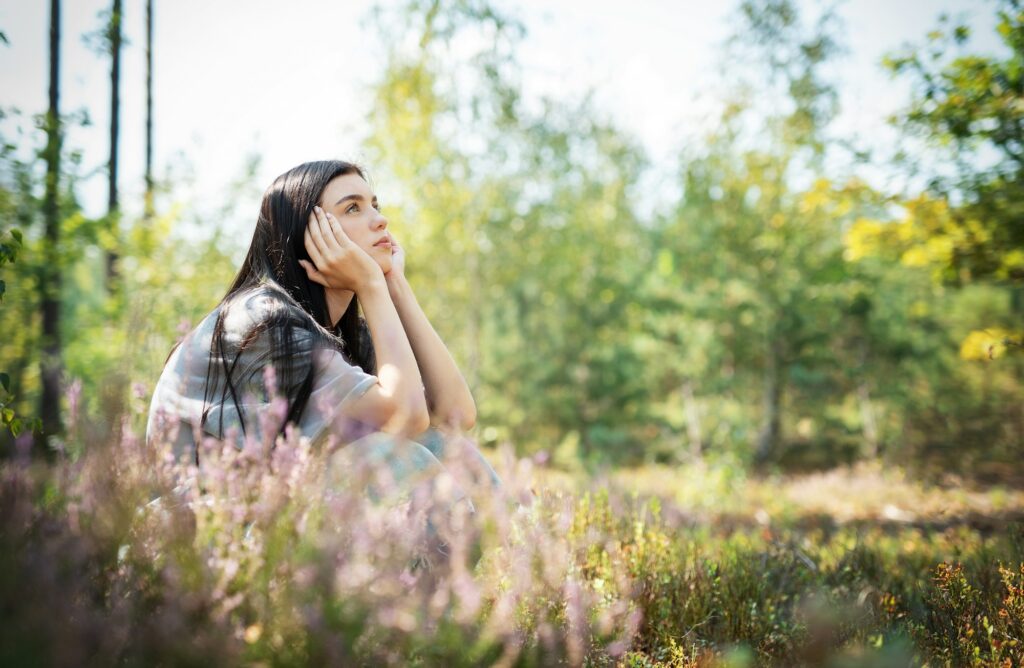 A young woman sits peacefully in a sunlit forest clearing, enjoying nature and reflecting