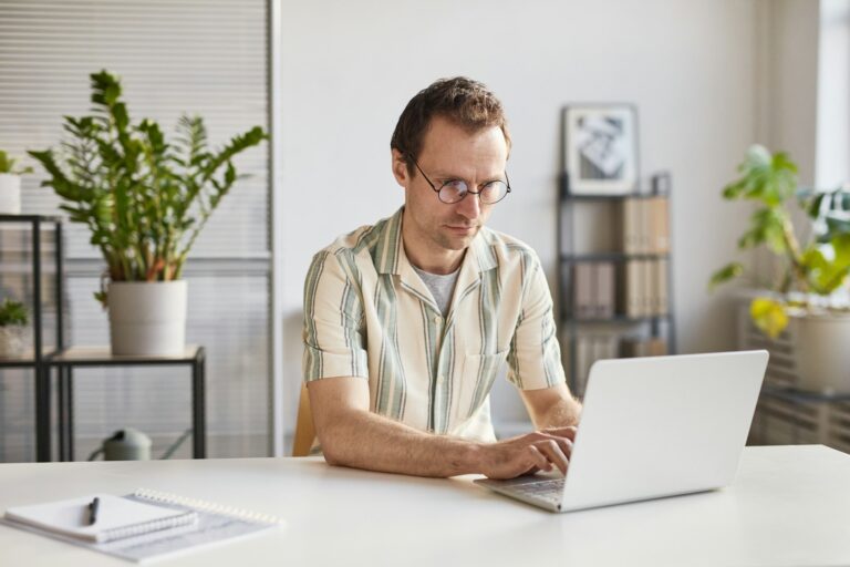 Man working on laptop, surrounded by plants and natural light.