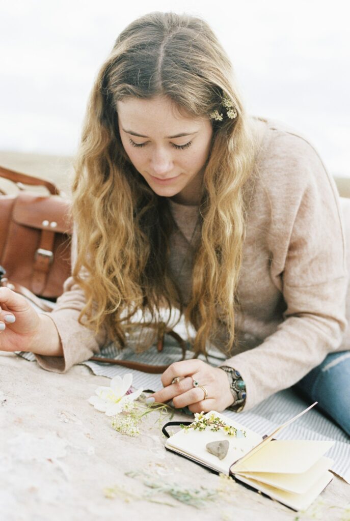 Woman sitting on a rock, putting wild flowers between the pages of a notebook.