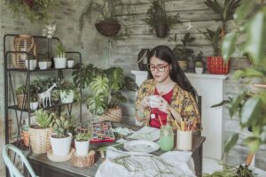 Young woan drinking tea and lookig at her paintings of plants